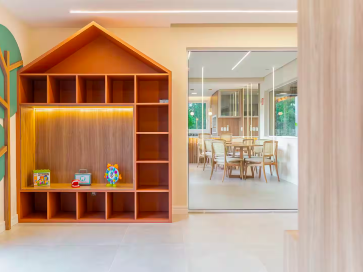 Brinquedoteca com estante em formato de casinha e salão ao fundo